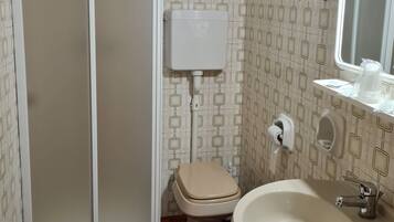 Baño con inodoro, bidé, lavamanos y ducha con puerta de vidrio.
