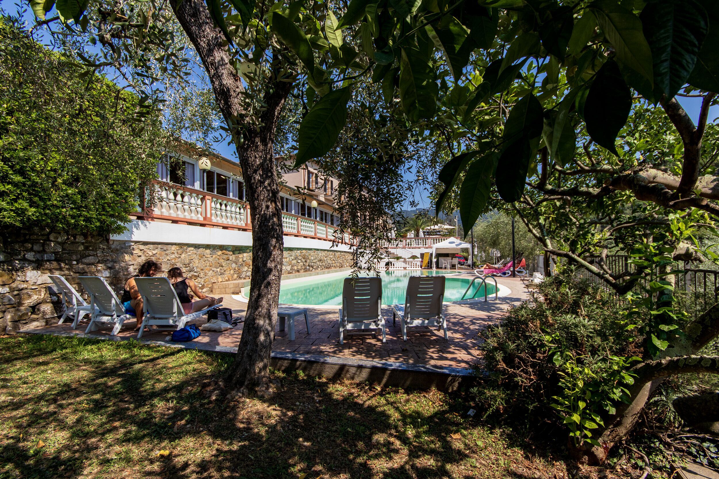 Zona junto a la piscina con sillas de descanso, una pared de piedra y un edificio con balcón al fondo.