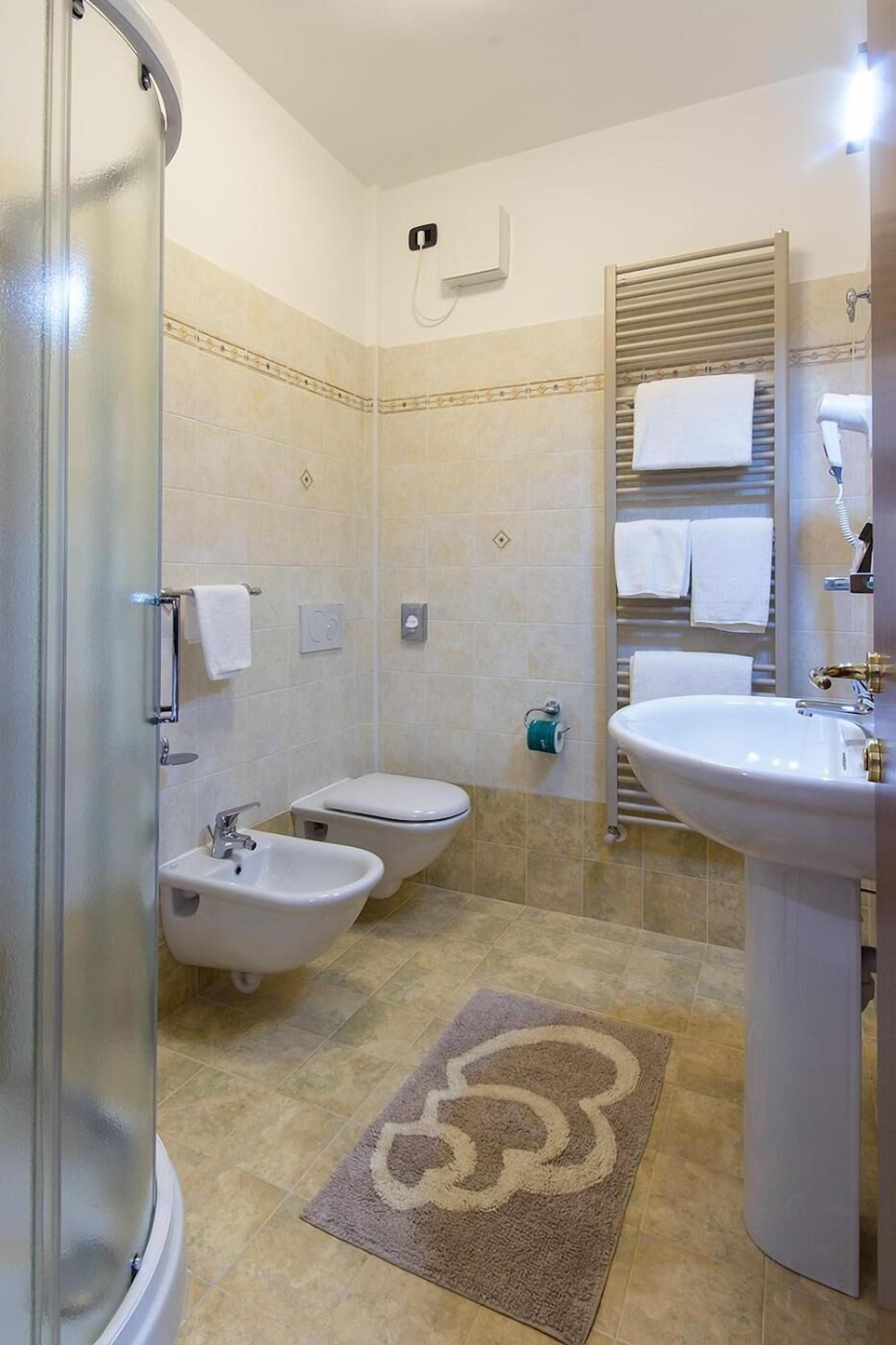 A bathroom with a shower, bidet, toilet, sink, and towel rack.