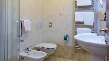 A bathroom with a shower, bidet, toilet, sink, and towel rack.