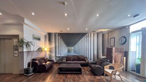 A spacious lobby with a long corridor, leather sofas, a small table, and a wicker chair. - Hôtel Le National (Sète)