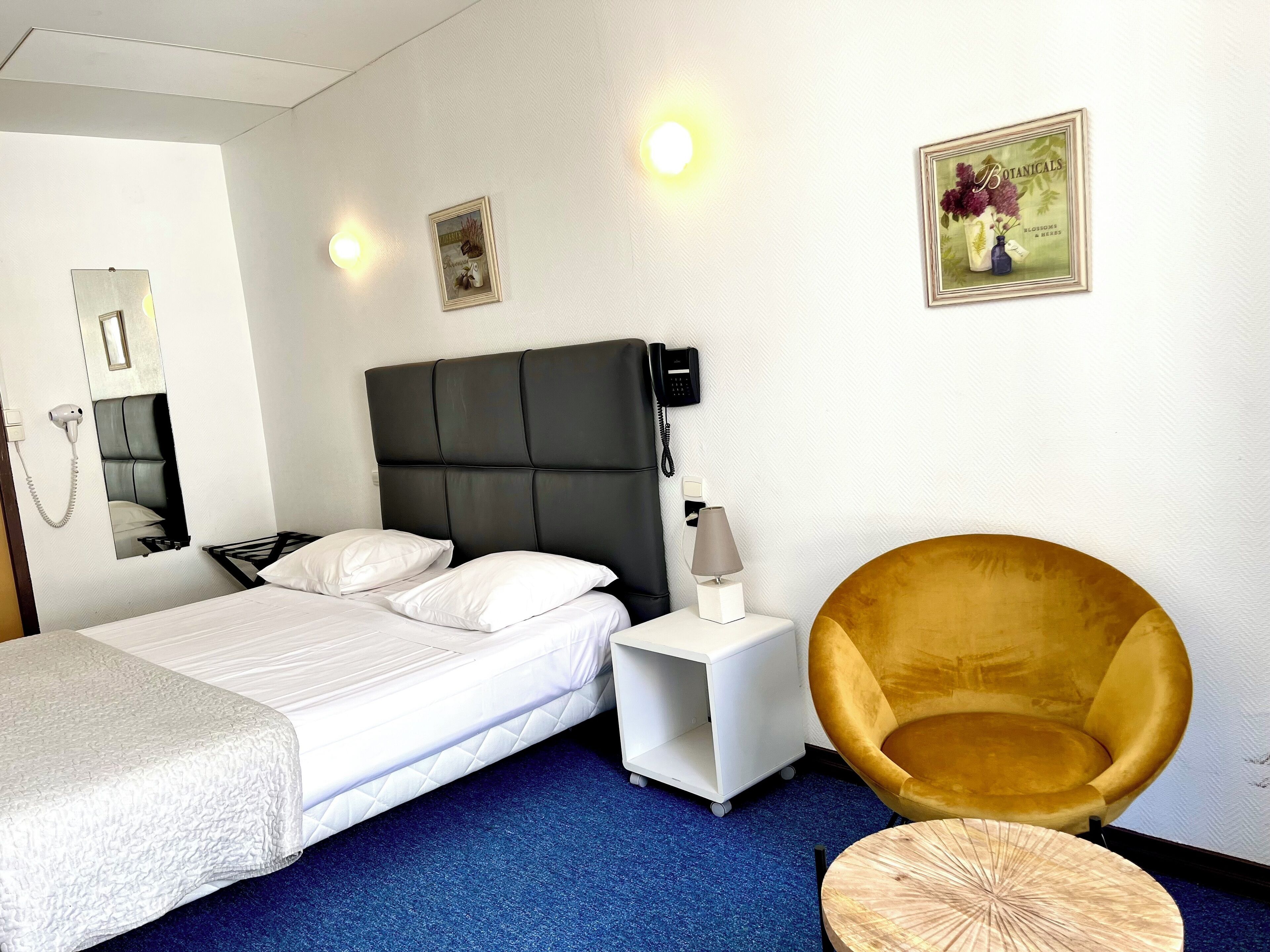 Una habitación de hotel con cama, mesita de noche, lámpara, silla y adornos en la pared.