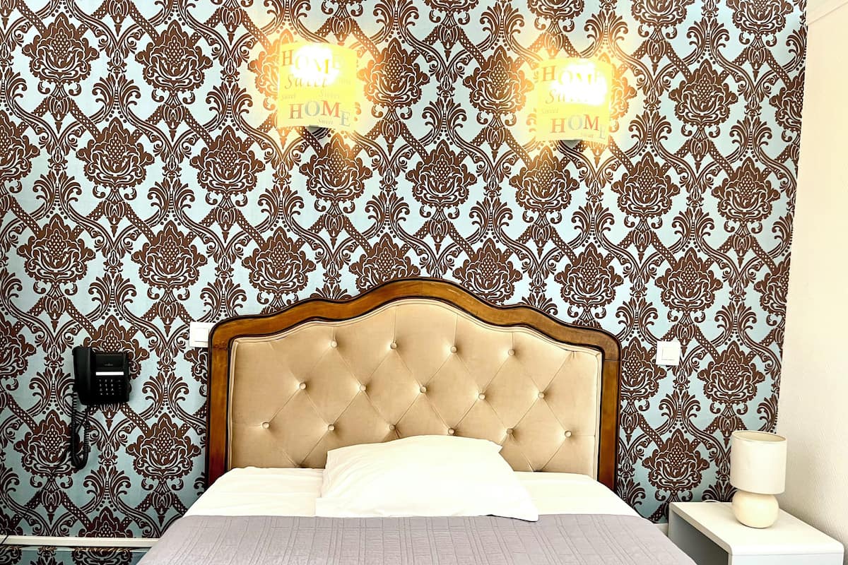 Un dormitorio con papel tapiz estampado, cabecero acolchado, lámpara de noche y teléfono.