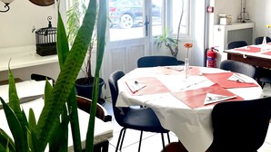 A dining area with a white table, blue chairs, and potted plants. - Hôtel Le National (Sète)