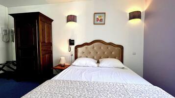 Habitación de hotel con cama, armario de madera, lámpara de noche, teléfono e iluminación en la pared.