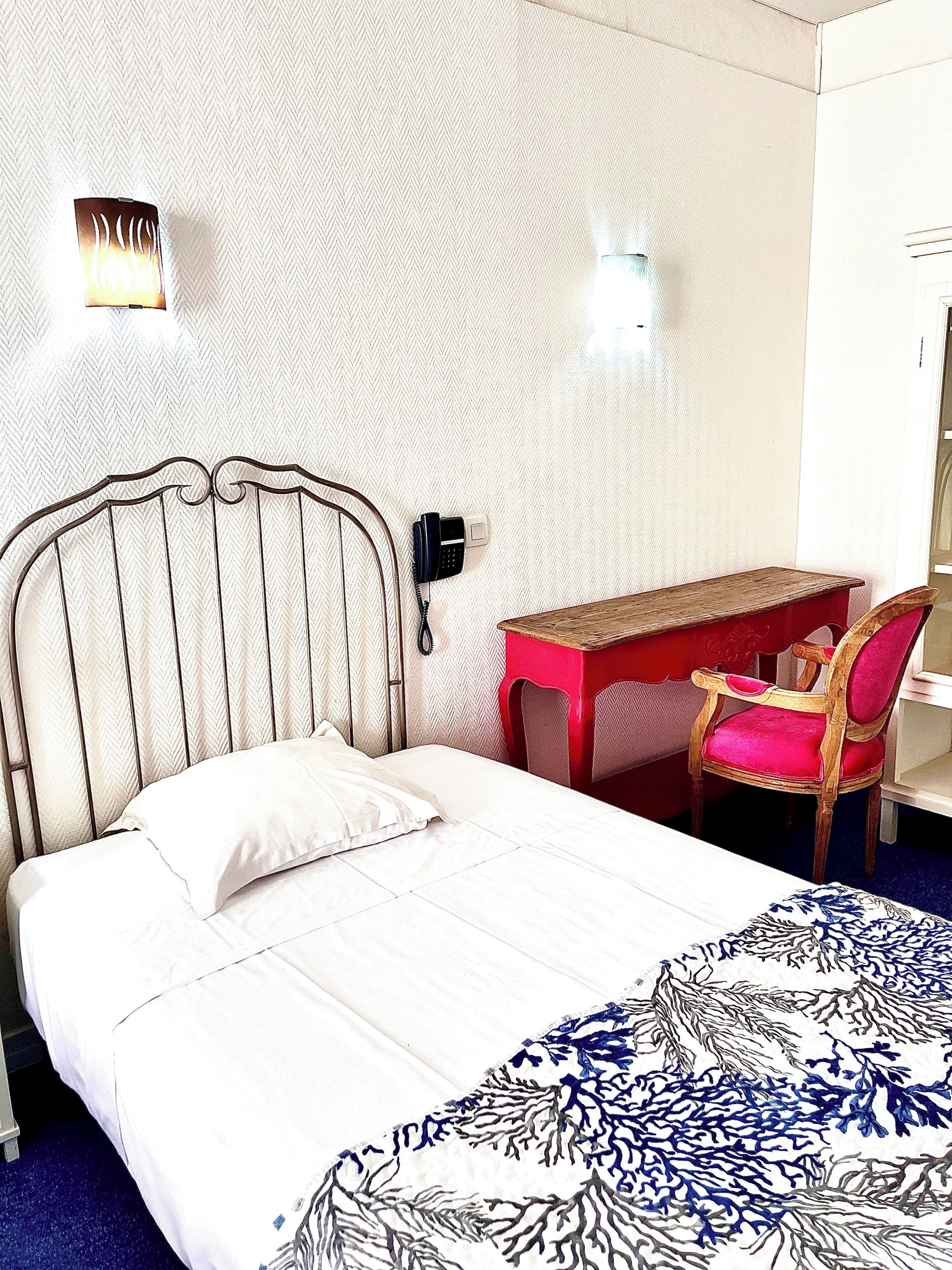 A hotel room with a bed, a desk, a chair, and a phone.