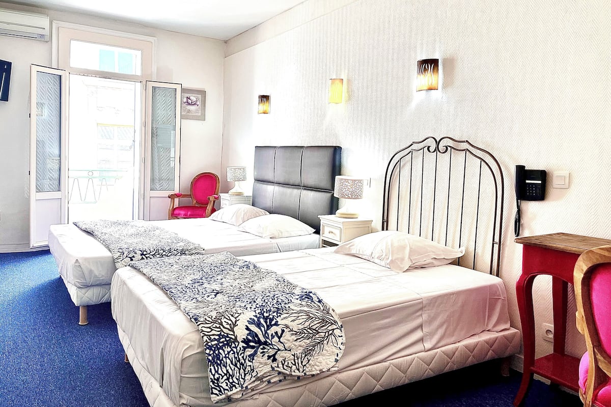 Habitación de hotel con dos camas, una silla roja, una mesita de noche con lámpara y un teléfono en la pared.