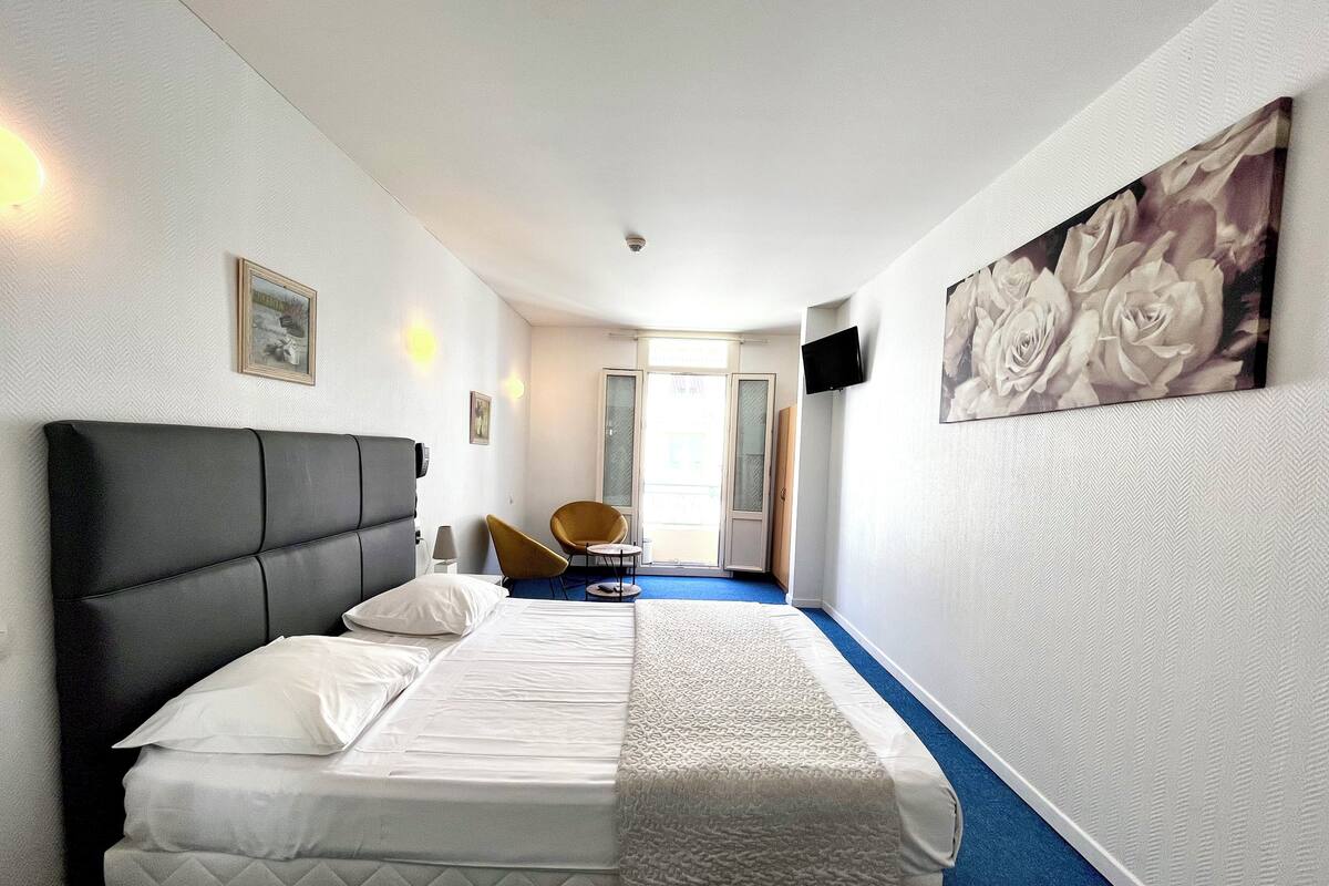 Una habitación de hotel con una cama, una silla, un televisor y un cuadro en la pared.