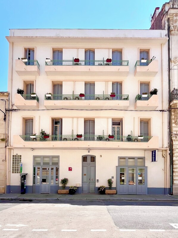 A multi-story hotel with balconies, a ground-level entrance, and a sign indicating it is a hotel. - Hôtel Le National (Sète)