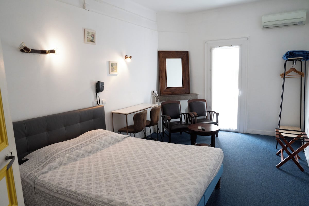 Habitación de hotel con cama, escritorio, dos sillas, espejo y perchero.