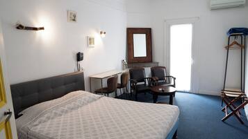 Habitación de hotel con cama, escritorio, dos sillas, espejo y perchero.