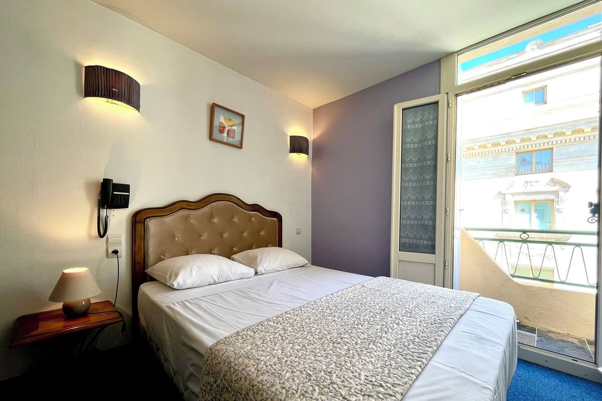 Habitación de hotel con cama, lámpara de noche, teléfono y vistas al exterior.
