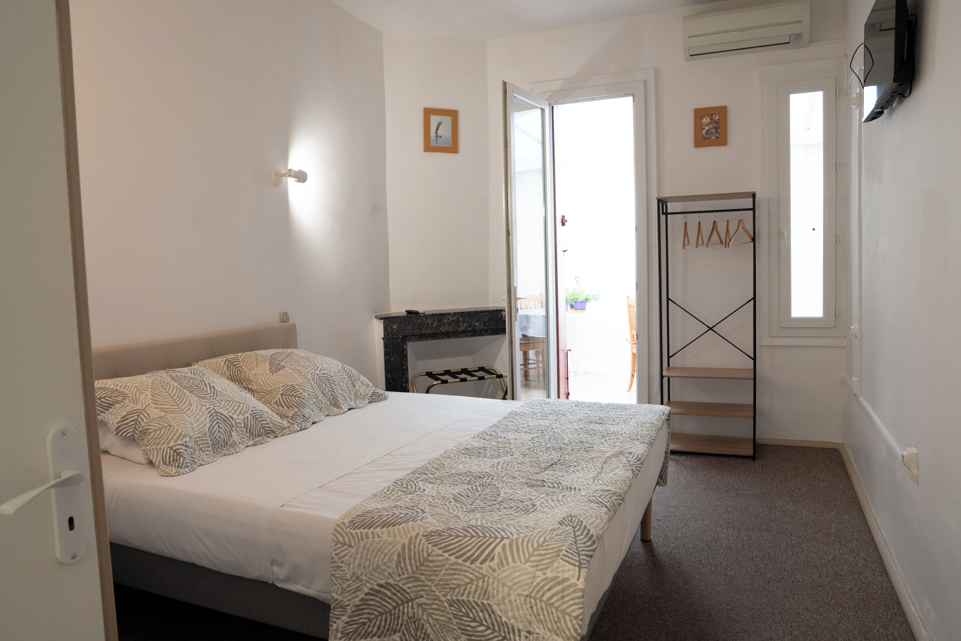 A bedroom with a bed, a wardrobe, a door leading to a balcony, and a wall-mounted TV.