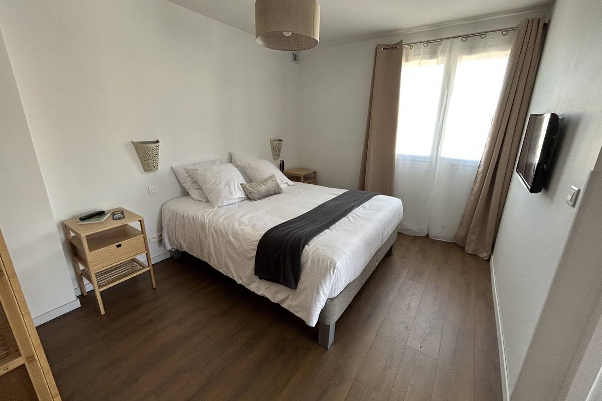 Un dormitorio con cama, mesitas de noche, televisor y ventana con cortinas.