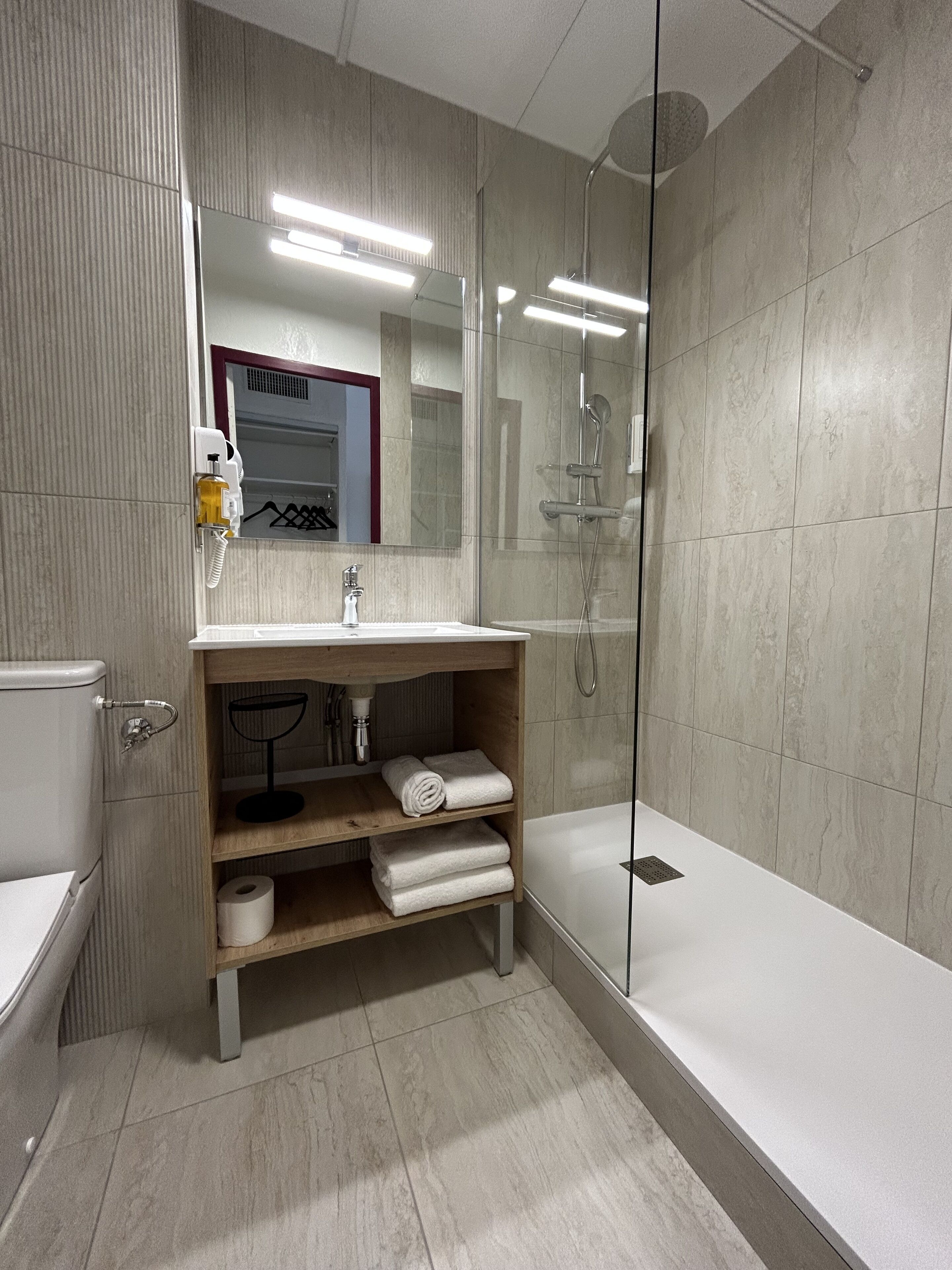 A modern bathroom with a glass-enclosed shower, a wooden vanity with a mirror, and a toilet.
