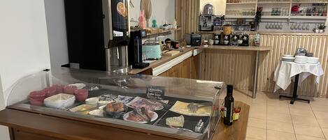 Zona de bufé con diversas opciones de comida, una máquina de café y una exhibición de cristalería.