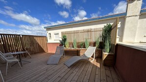 A wooden deck with two lounge chairs and a small table, surrounded by wooden planters and a fence.