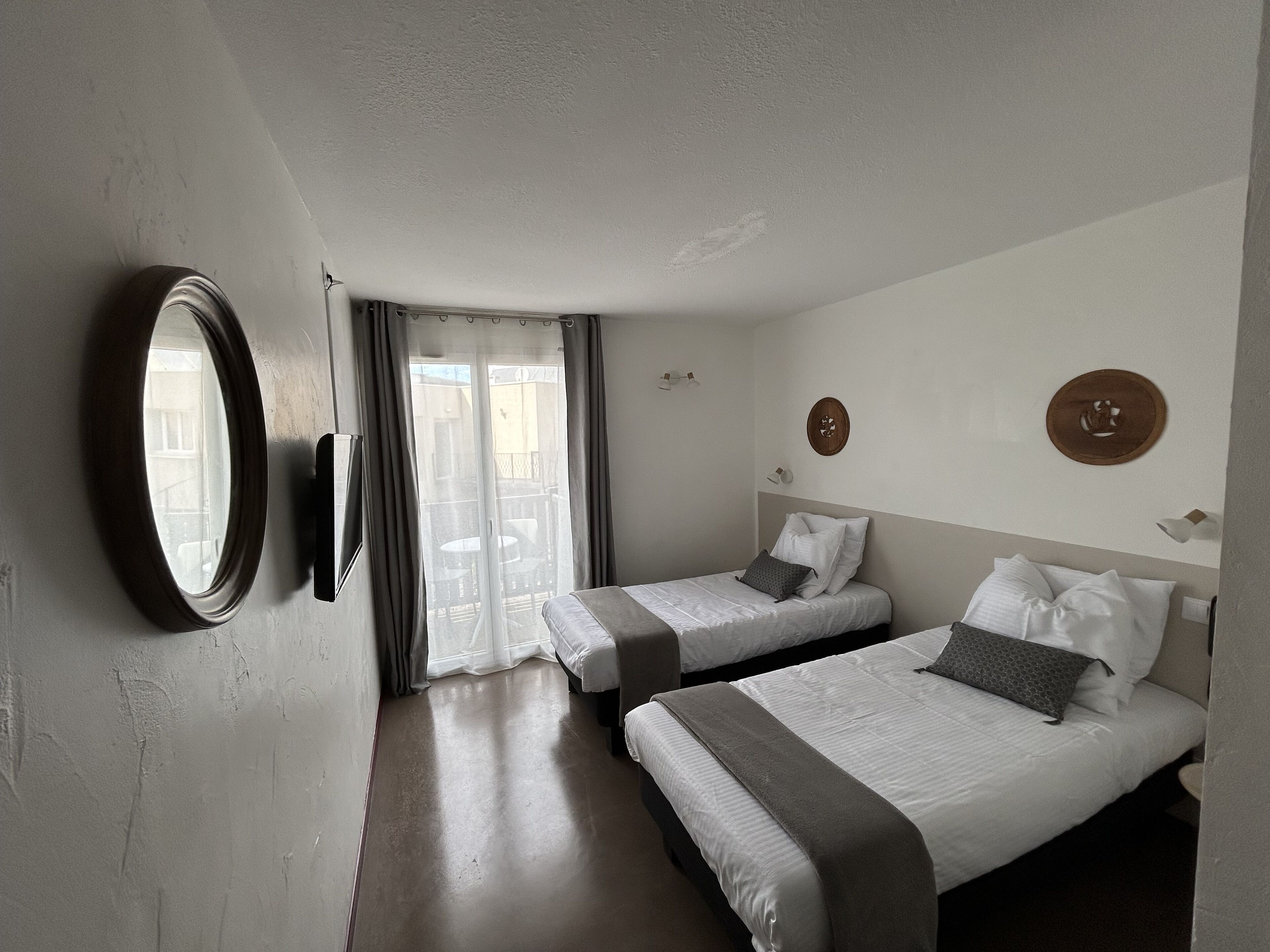 Quarto de hotel com duas camas, um espelho grande e porta de vidro deslizante para a varanda.