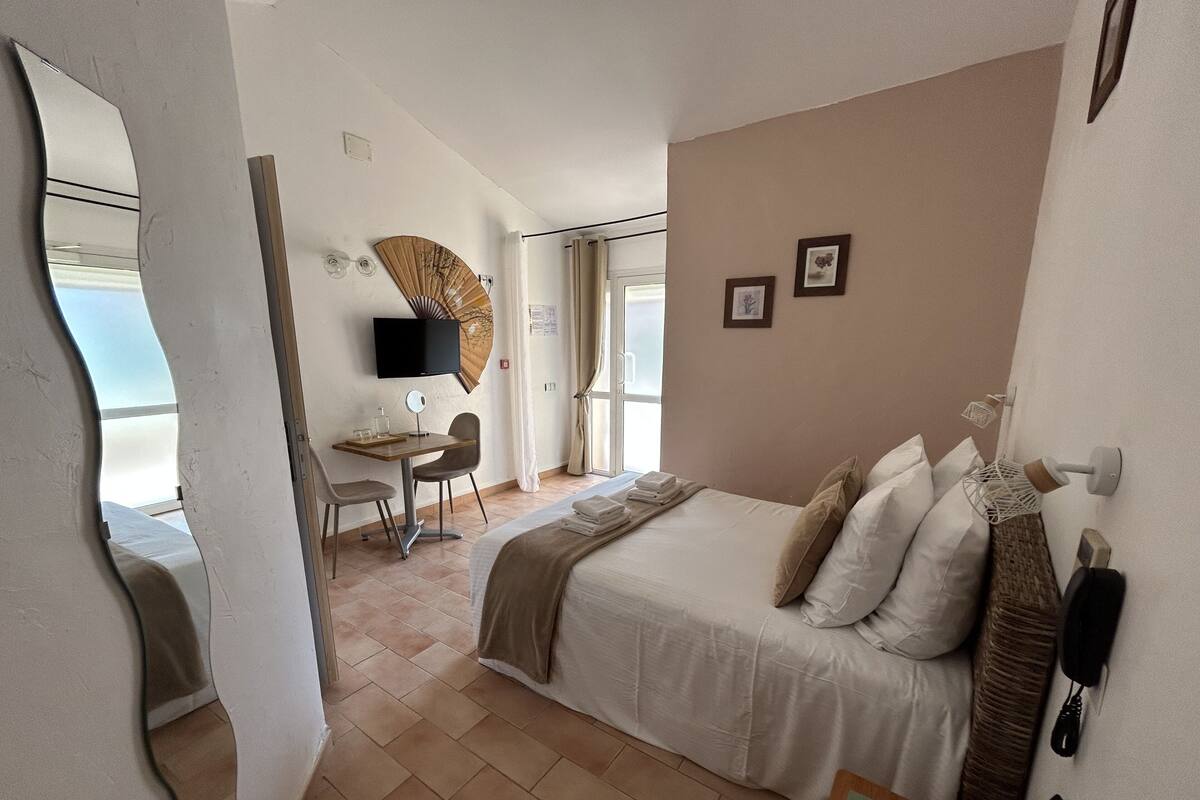 Una habitación de hotel con cama, escritorio, silla, televisor y ventana.