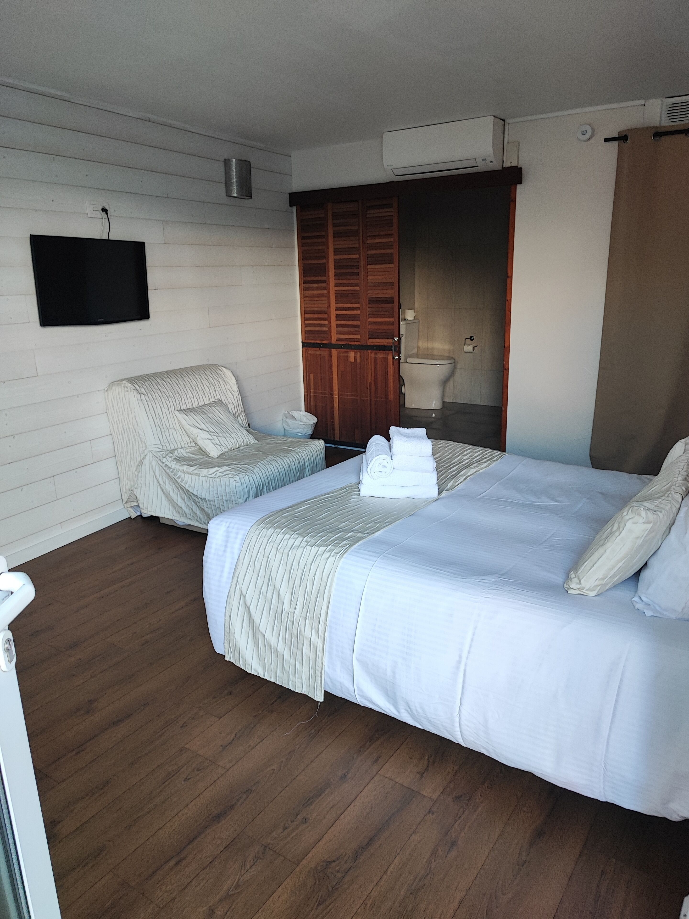 Une chambre d’hôtel avec un grand lit, une chaise, une télévision et une armoire.
