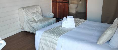 A hotel room with a large bed, a chair, a television, and a wardrobe.