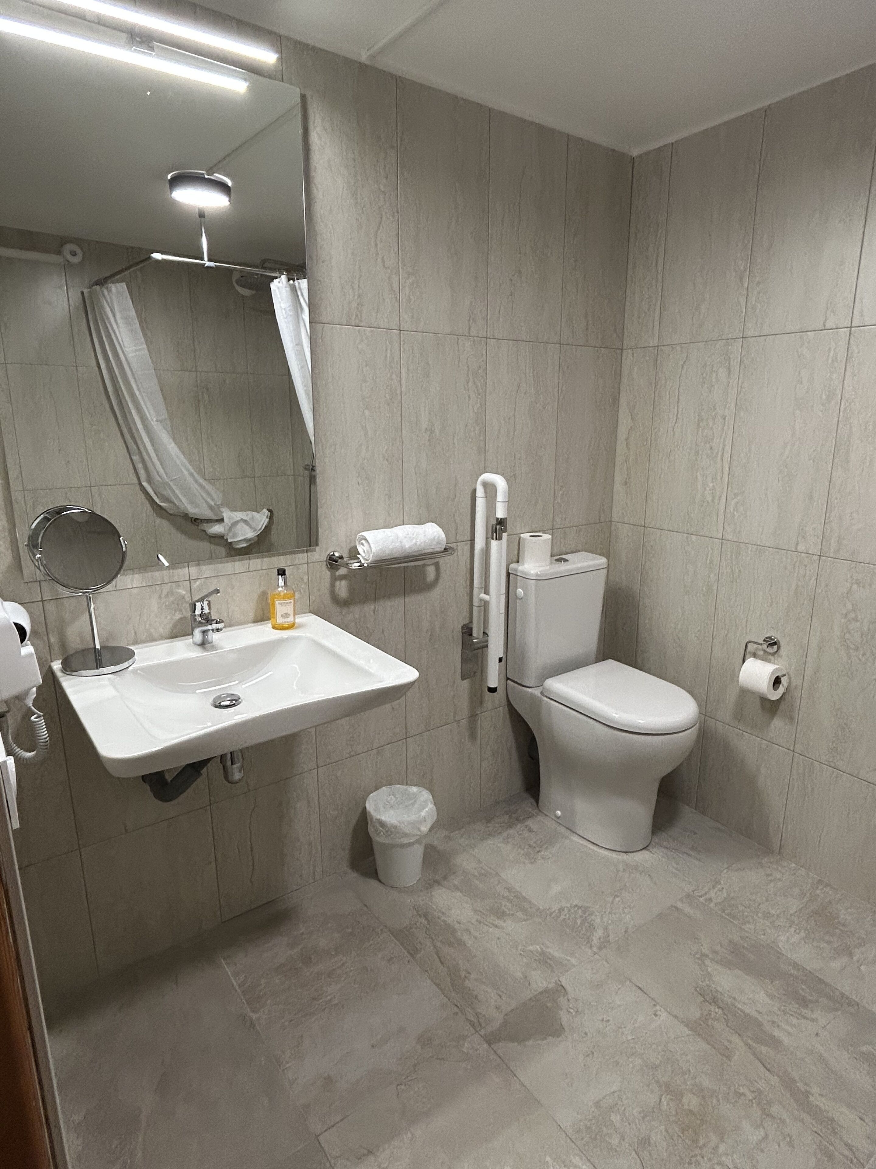 A modern bathroom with a white sink, mirror, toilet, and a trash bin.