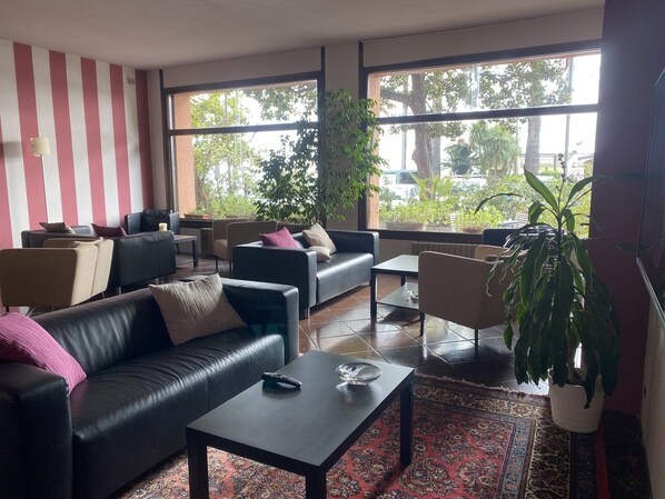 Una sala de estar moderna con un sofá de cuero negro, una mesa de centro y una alfombra estampada. Ofrece múltiples opciones de asientos, incluyendo un sofá y sillones. Amplias ventanas ofrecen vistas al exterior.