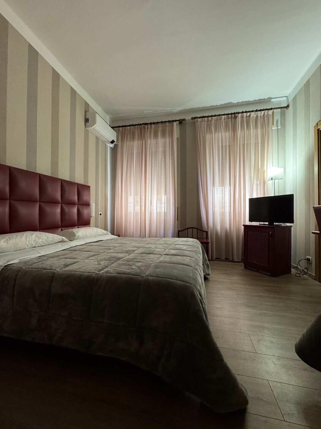 Quarto de hotel com uma cama grande, um móvel para televisão e cortinas.
