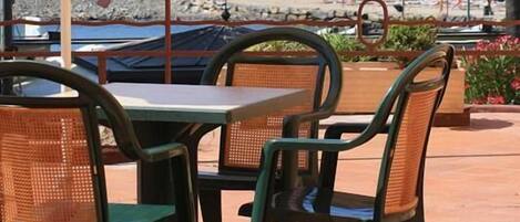 Un espacio al aire libre con mesas y sillas, con vistas a un litoral rocoso y al mar.