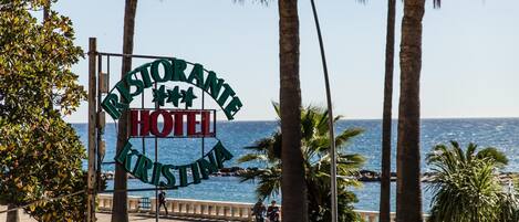 A sign for a hotel named "Ristorante Krisztina" with a view of the sea and palm trees.