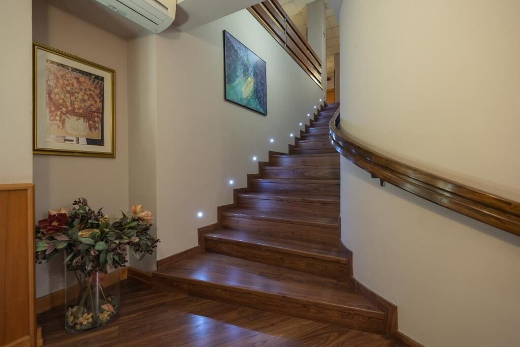 A wooden staircase with a handrail, a vase of flowers, and two framed artworks on the walls.