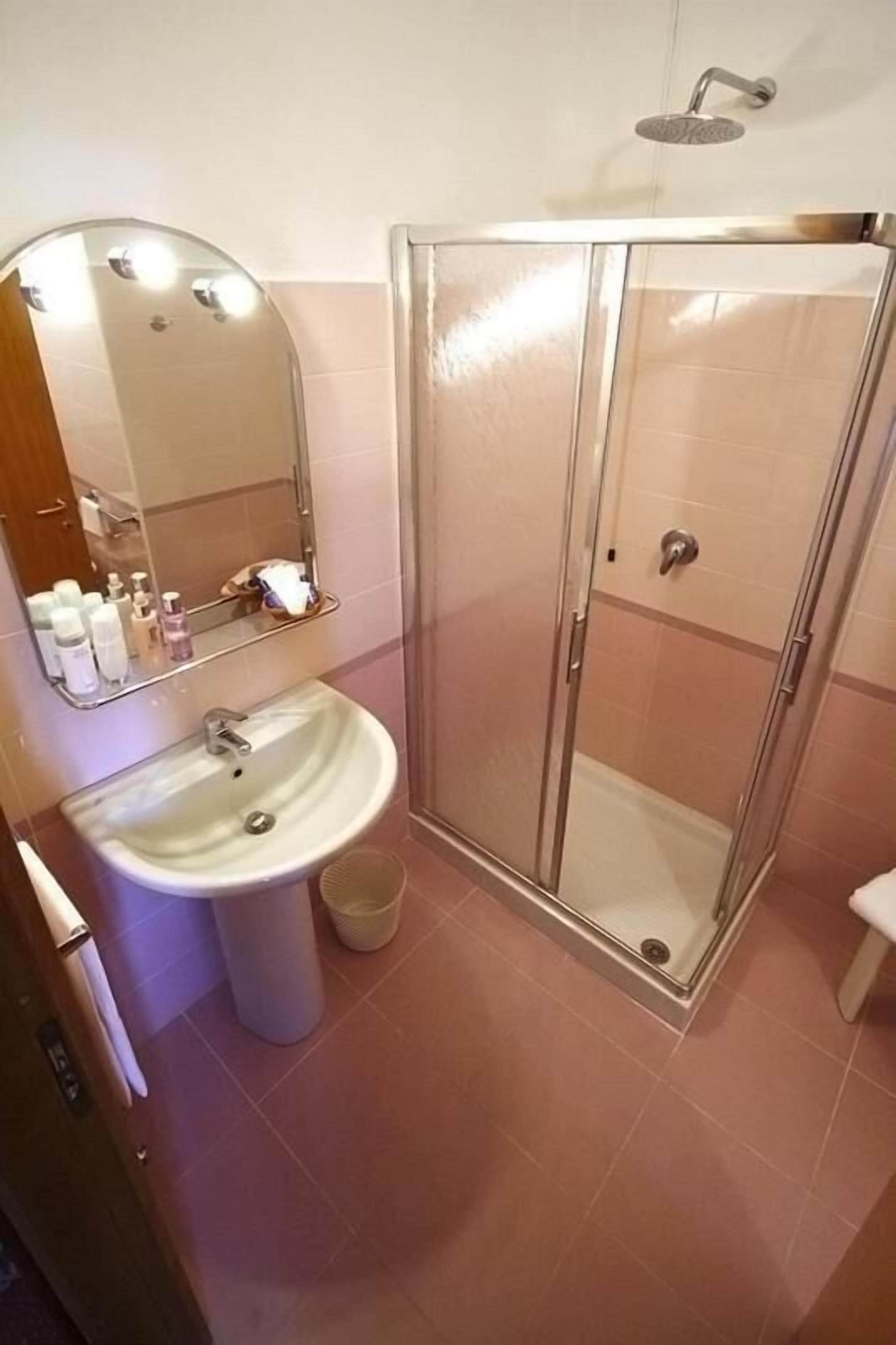 Une salle de bain avec une douche à parois de verre, un lavabo avec un miroir et une poubelle.