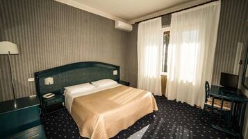Ein Hotelzimmer mit Bett, Schreibtisch, Stuhl, Lampe und Vorhängen.