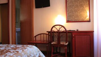 A hotel room with a bed, a desk, a chair, a television, and a mirror.