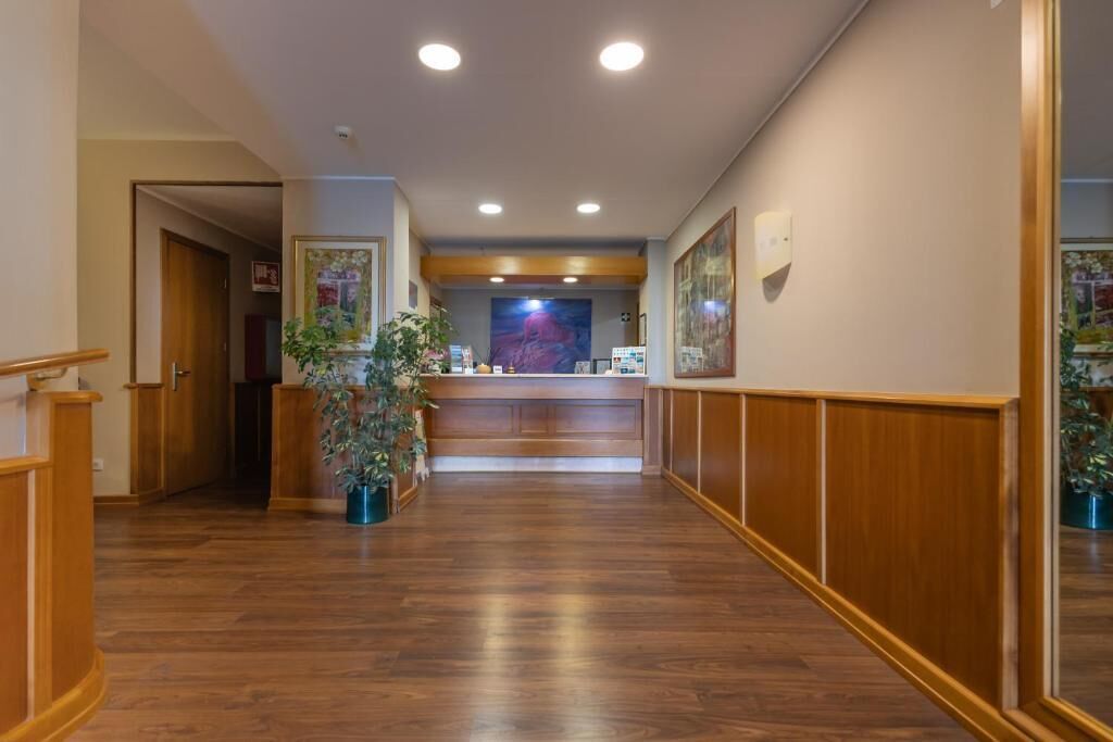 A hotel lobby with wooden flooring, a reception desk, and framed artwork on the walls.