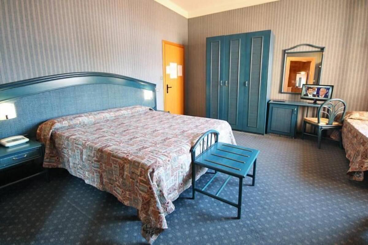 Ett hotellrum med en säng, ett skrivbord, en stol, en garderob och en spegel.