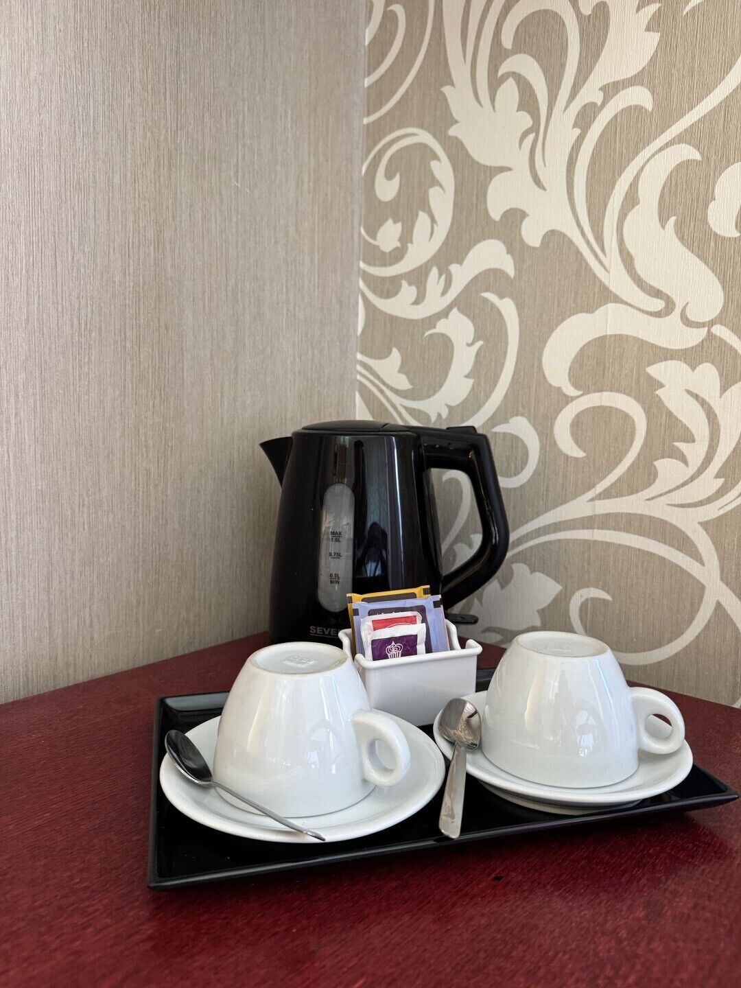 A table with a coffee maker, two cups, a tray, and a spoon.