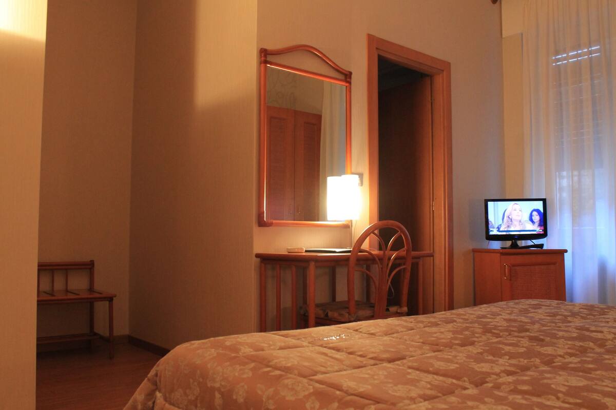Ett hotellrum med en säng, en tv, ett skrivbord med en stol och en spegel.