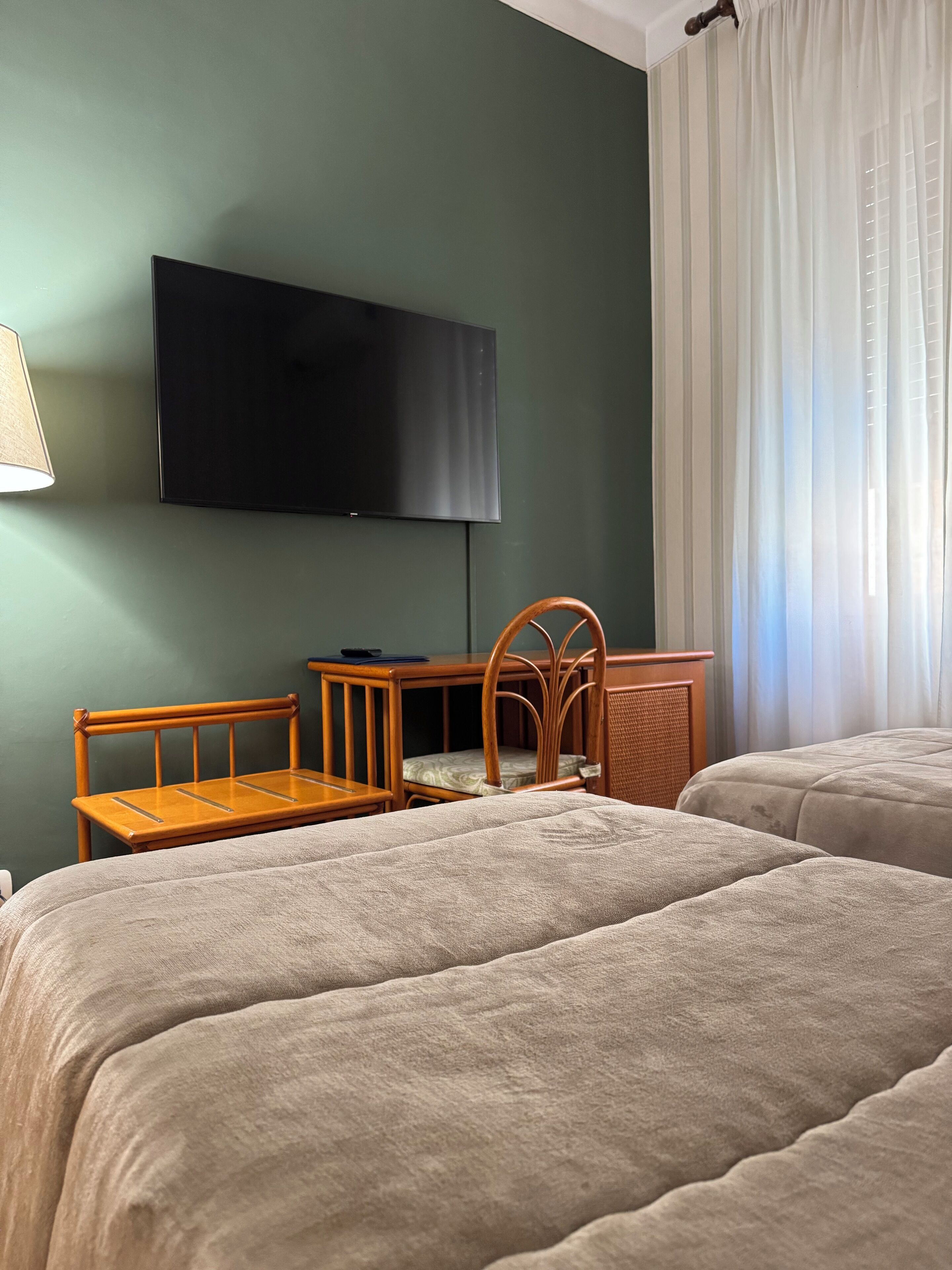 Hotelkamer met twee bedden, een bureau, een stoel, een televisie en een raam met gordijnen.