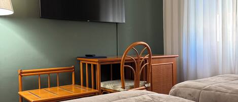 Ein Hotelzimmer mit zwei Betten, einem Schreibtisch, einem Stuhl, einem Fernseher und einem Fenster mit Vorhängen.