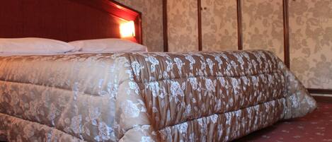 A bed with a floral-patterned duvet in a room with floral wallpaper and wooden paneling.