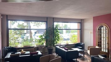 A spacious lobby with large windows, comfortable seating, and a potted plant.