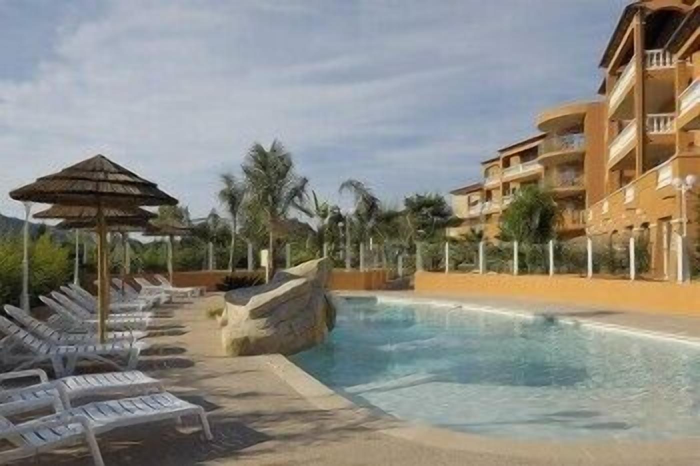 Poolbereich eines Resorts mit Liegestühlen, einer kleinen Felsformation und einer Palme.