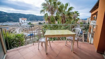 A balcony with a table and chairs, overlooking a cityscape and hills.