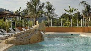 Une piscine bordée de chaises longues, un ensemble de rochers et une végétation tropicale.