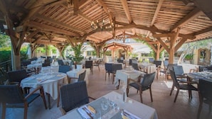 Un espace de restauration en plein air agrémenté de pergolas en bois, de tables recouvertes de nappes blanches et de chaises en osier.