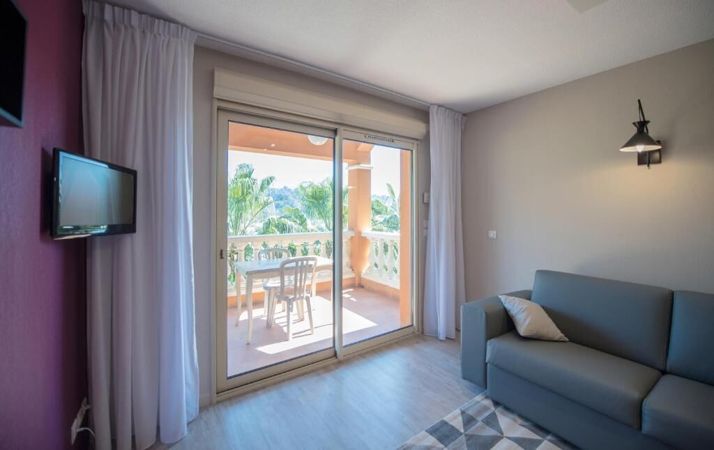 A room with a sofa, a TV, a sliding glass door to a balcony, and a lamp.