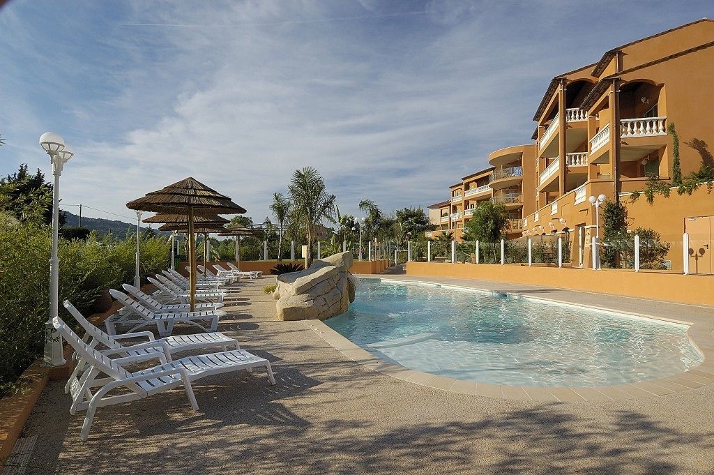 A resort pool area with lounge chairs, umbrellas, and a building with balconies.