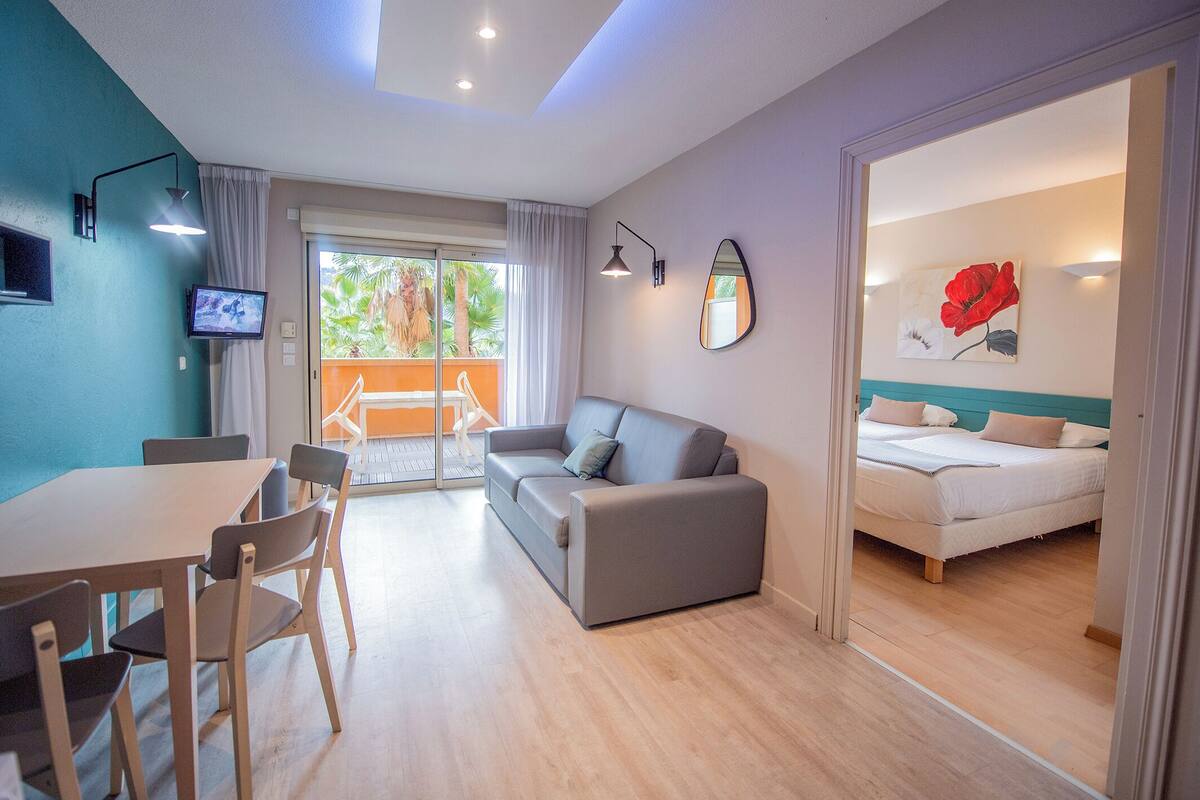 A modern hotel room with a balcony, a dining area, and a bedroom.
