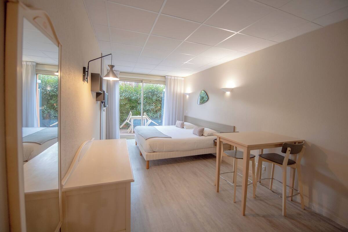 A modern hotel room with a bed, bedside table, and a desk with chairs.
